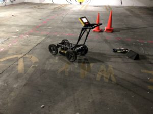 Operational ground-penetrating radar unit with marking paint and traffic cones on a concrete floor, used for 'Dig Alert and GPR' to ensure safety in underground excavations.