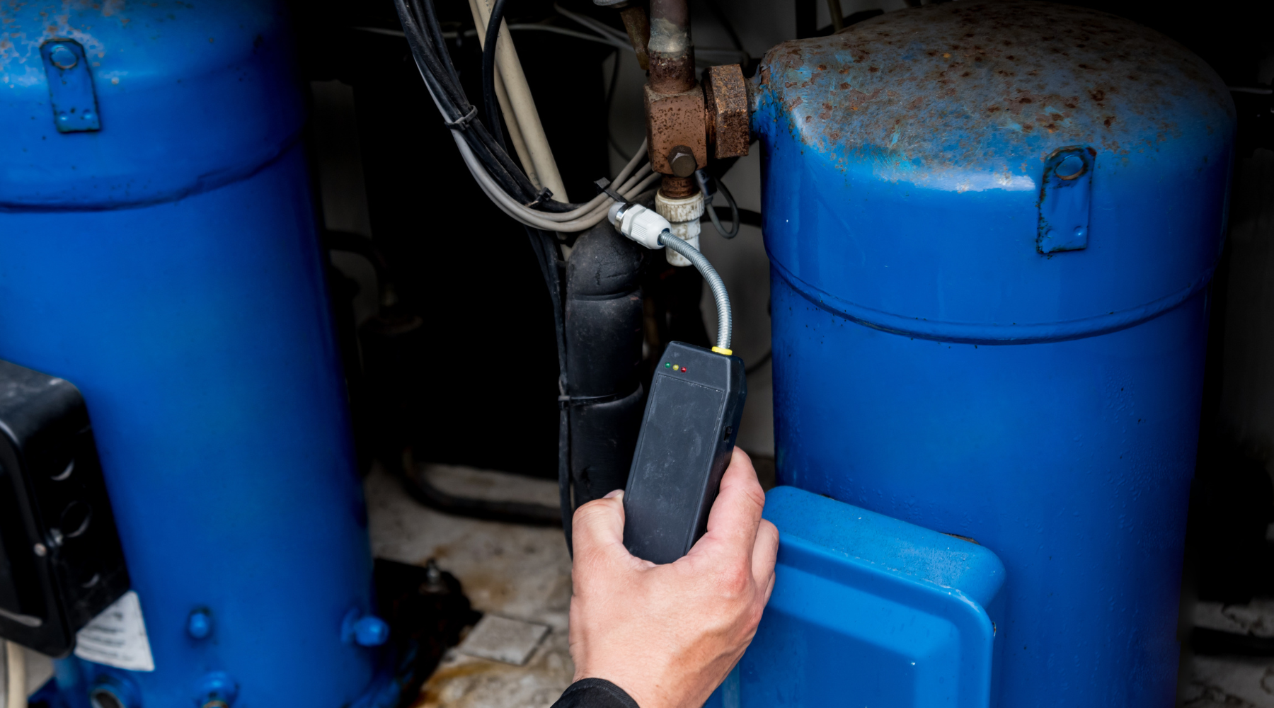 A hand using an infrared methane tester near blue tanks, comparing catalytic vs infrared methods.